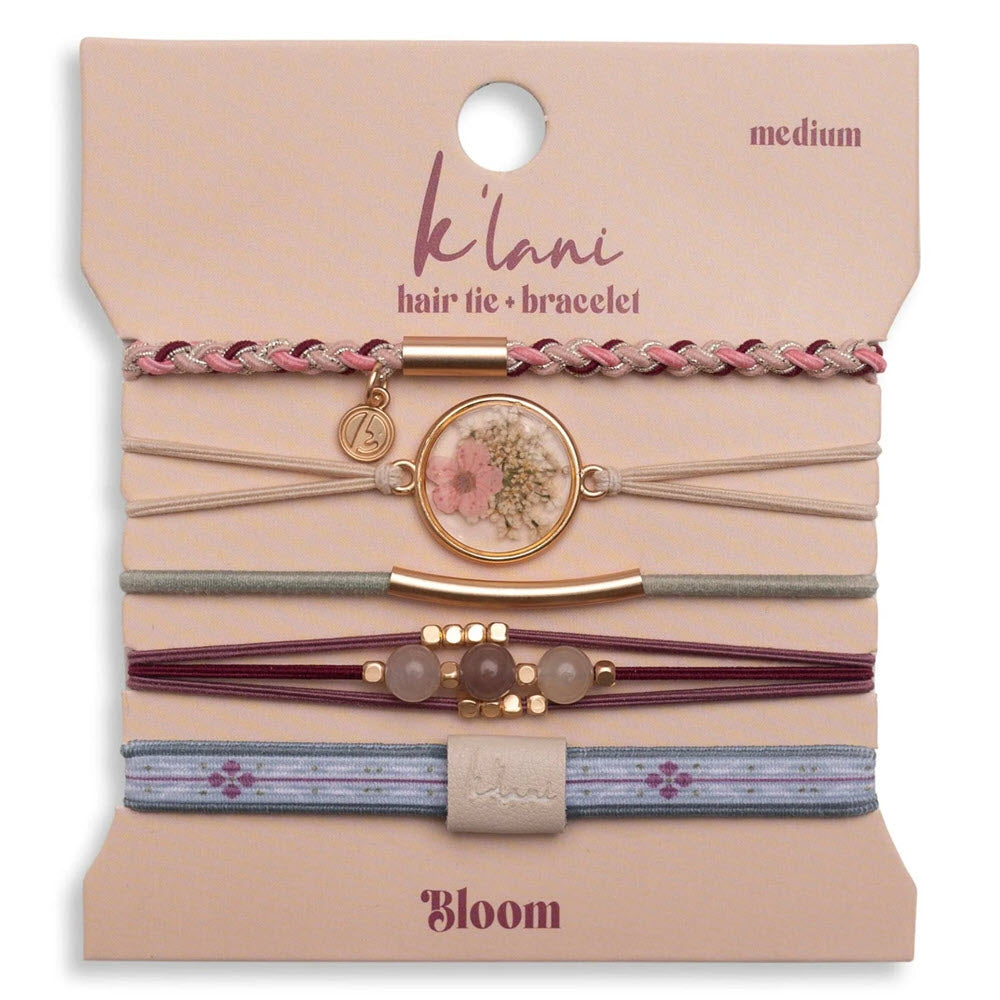 Five assorted hair ties and bracelets in pink, gold, and purple tones are displayed on a card labeled klani hair tie + bracelet, medium, Bloom. The set features floral and bead accents.