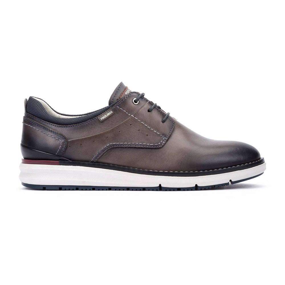 A single brown leather lace-up dress shoe with a white and black rubber sole, subtle red accent on the heel, and fine stitching details, viewed from the side.