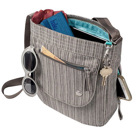 A gray Haiku Jaunt Crossbody Bag with personal items like a phone, sunglasses, wallet, and keys in the main compartment.