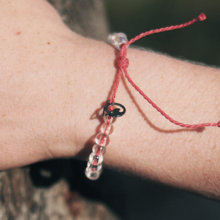 A 4Ocean Coral Reef bracelet with clear beads and a black charm, representing endangered coral reefs, on a person&#39;s wrist.