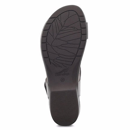 A sole of a Dansko Reece Waxy Burnished Stone sandal with leaf pattern tread and the brand logo &quot;Dansko&quot; visible.