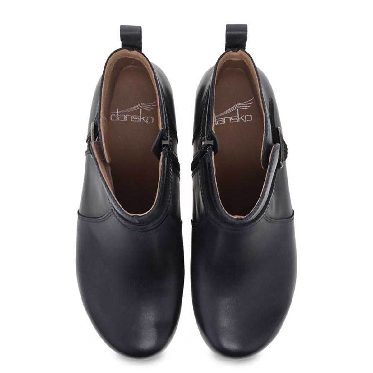 A pair of black leather slip-on shoes featuring Dansko Natural Arch technology, with a Dansko brand label on the insole, presented in a top-down view.