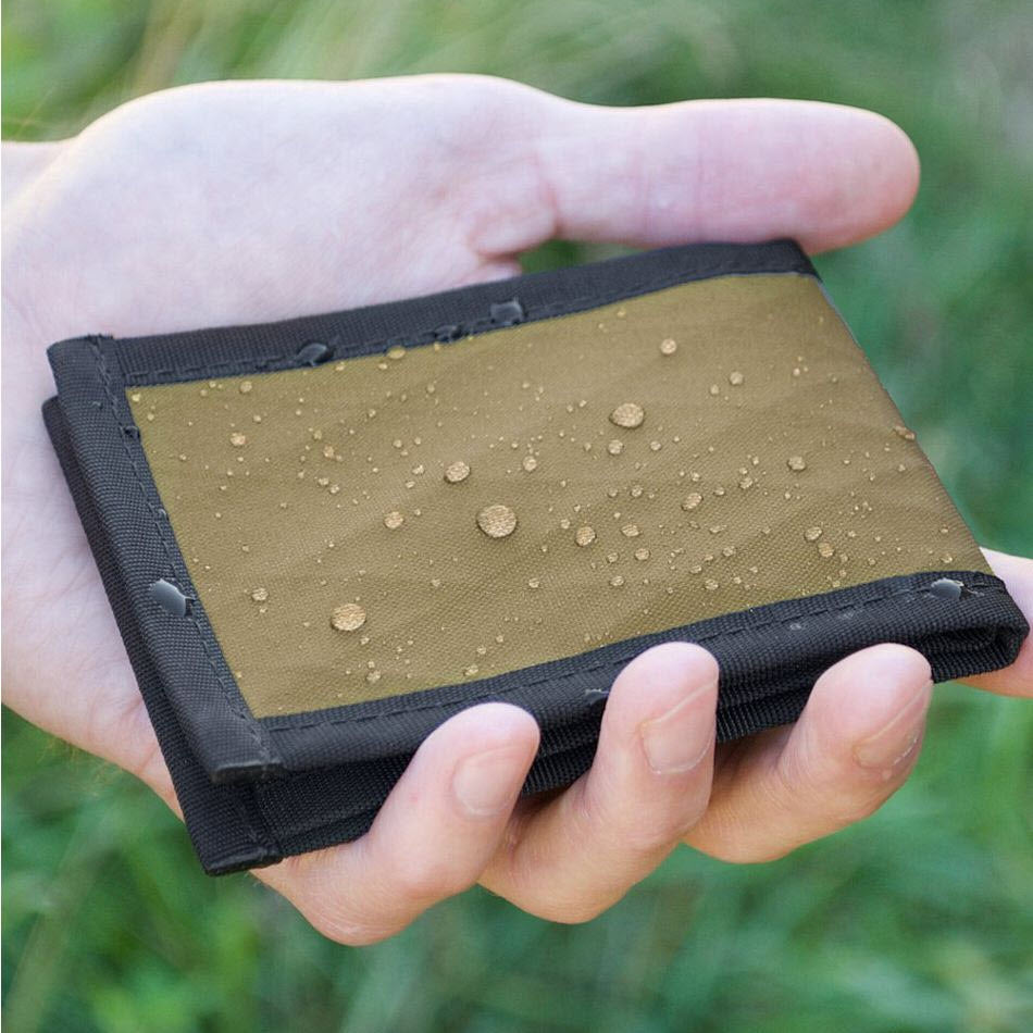 A hand holding a Flowfold Vanguard Wallet Olive made of water resistant outdoor fabric, with droplets on its surface.