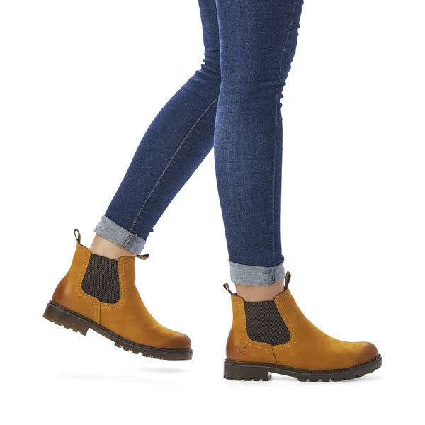 A person walking in Remonte Lug Bottom Chelsea Amber Boots paired with blue jeans against a white background showcases an on-trend style.