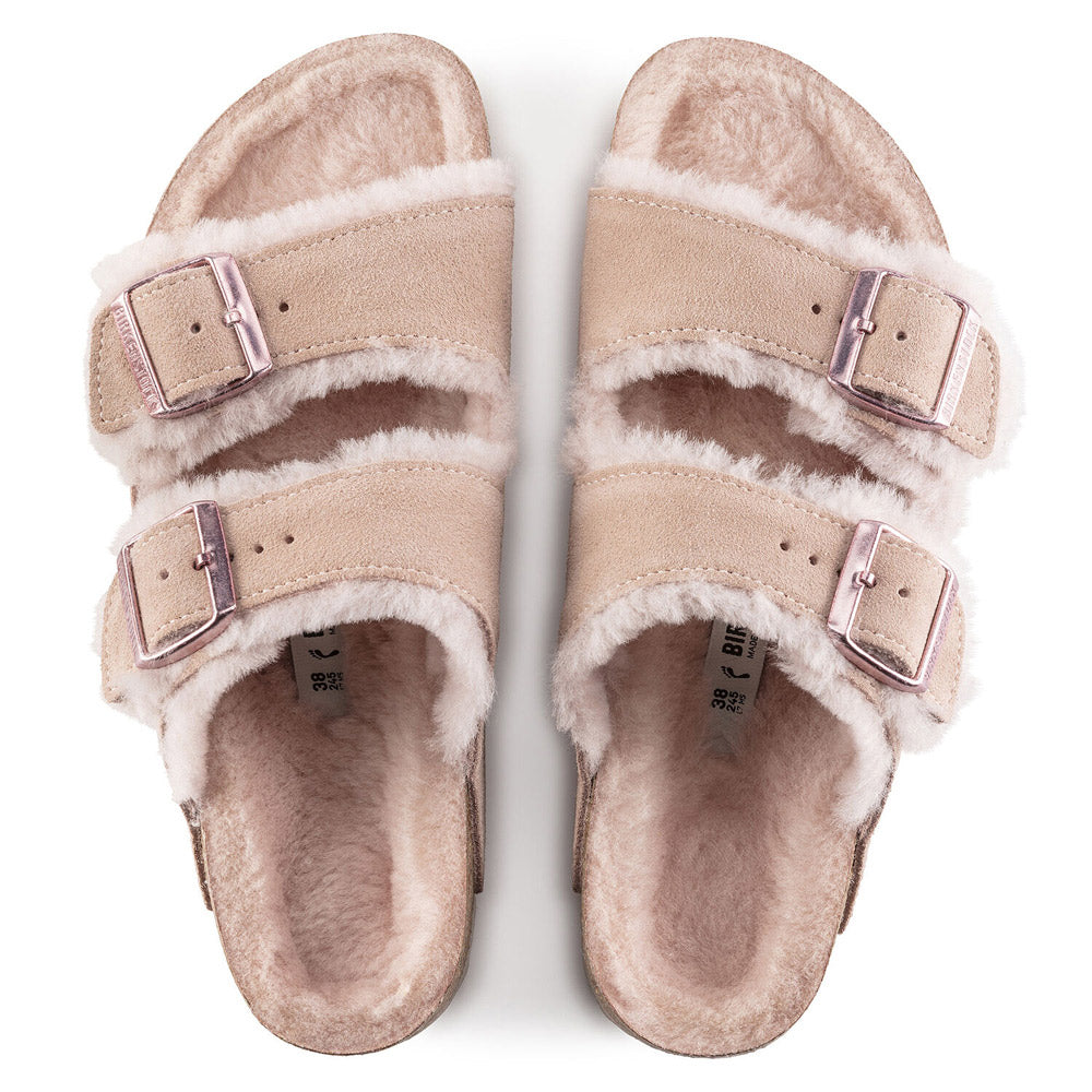 A pair of fluffy, beige-colored Birkenstock Arizona Shearling Light Rose slippers with adjustable straps and a cork-latex footbed on a white background.