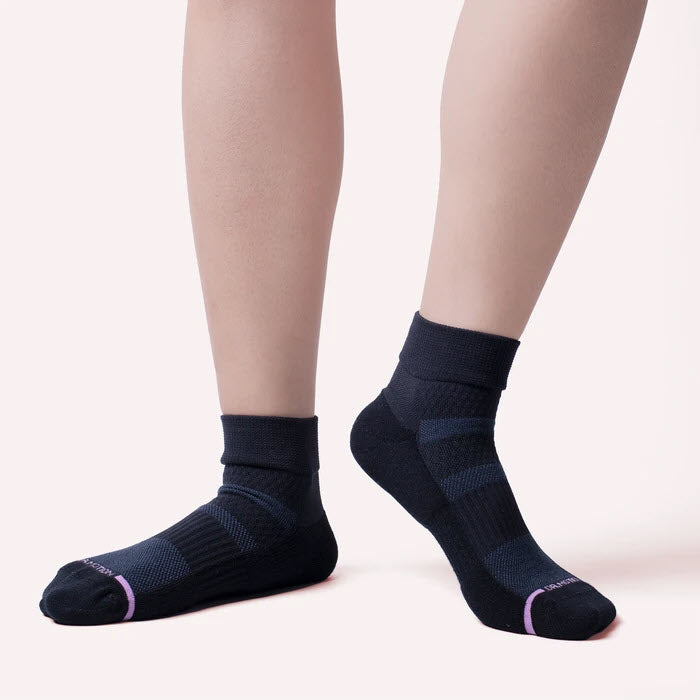 A person standing in Dr. Motion black anti-microbial ankle socks against a pale background.