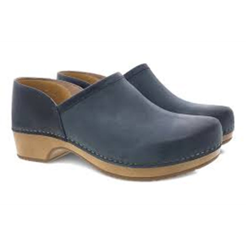 A pair of dark blue Dansko Brenna Navy Burnished clogs with wooden soles on a white background.