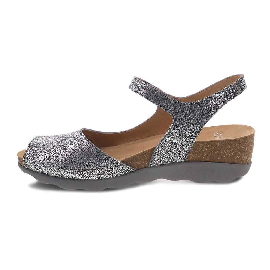 A single Dansko Marcy Pewter Metallic glittery women&#39;s Wedge Sandal with an adjustable ankle strap and a cork sole, isolated on a white background.