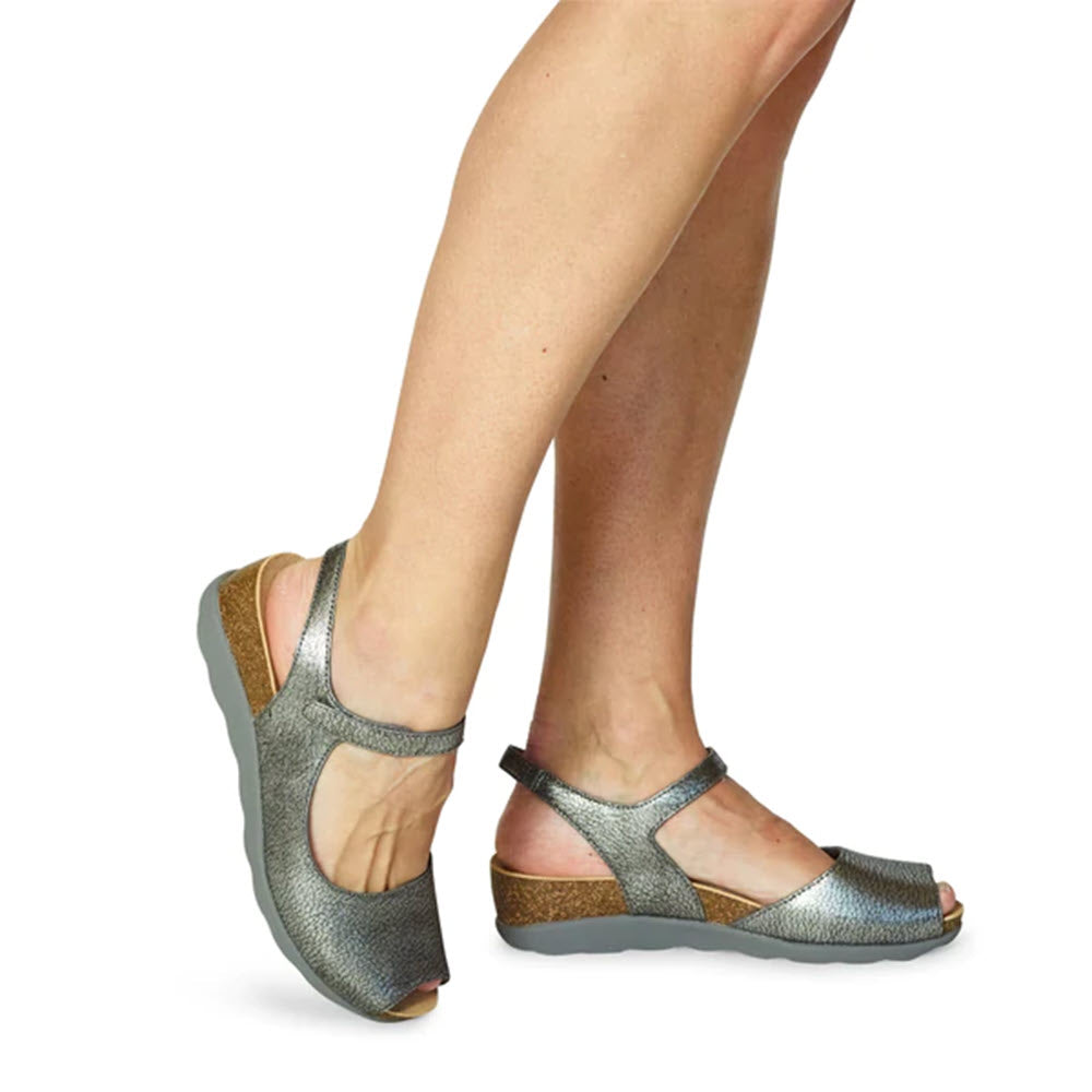 A pair of Dansko Marcy pewter metallic sandals with an adjustable ankle strap, shown from the calves down.