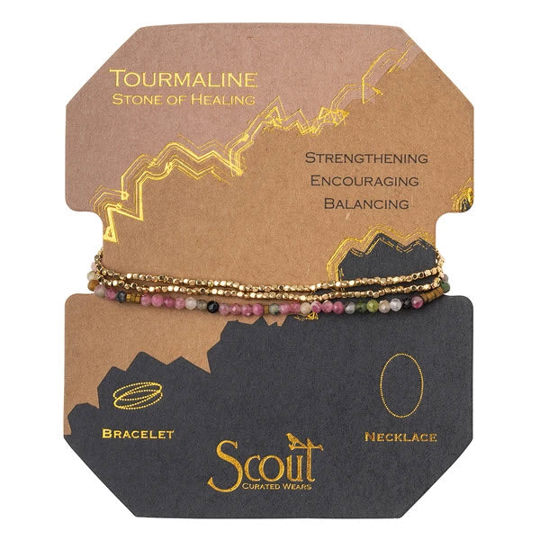 SCOUT DELICATE STONE WRAP BRACELET TOURMALINE/GOLD display with descriptions for tourmaline, the stone of healing, featuring bracelets and a necklace, with attributes such as strengthening, encouraging, and balancing.