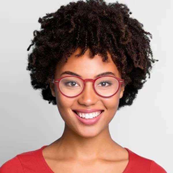 Smiling young woman with ICU Eyewear reading glasses round in red purple/teal and curly hair against a light background.