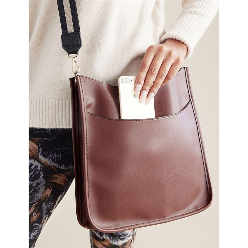 A person slipping a smartphone into a COCO &amp; CARMEN CONTRAST STRAP MESSENGER CHOCOLATE with a contrast strap.
