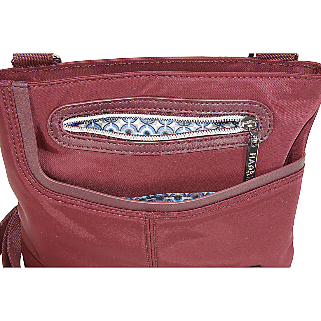 Close-up of a maroon Hadaki Mini Me Crossbody Wine with a zippered front pocket showing a patterned fabric lining.