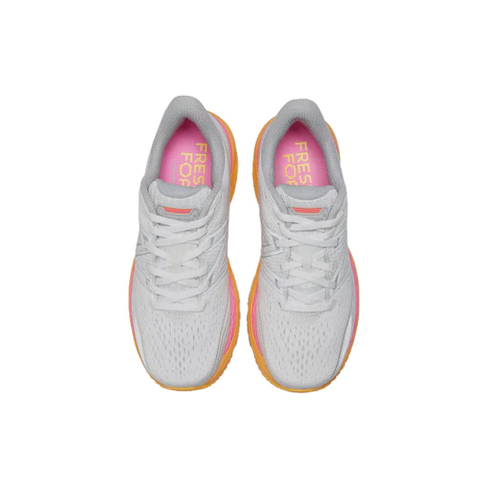 A pair of New Balance 860v12 white stability running shoes with pink and yellow accents, viewed from above, displayed on a plain white background.