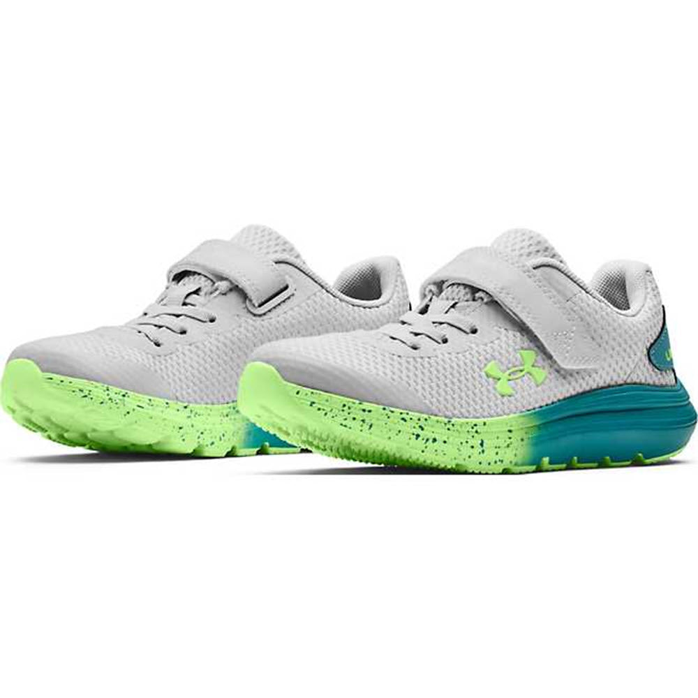 A pair of Under Armour Surge 2 AC Halo Grey - Kids athletic shoes with neon green soles and blue Under Armour brand logos.