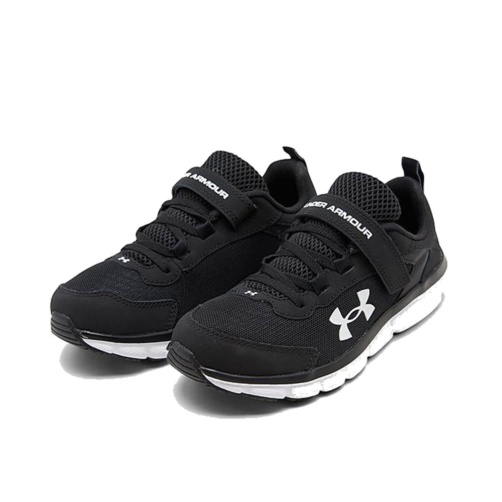 A pair of black Under Armour Assert 9 kid&#39;s athletic shoes with lightweight mesh upper and white soles.
