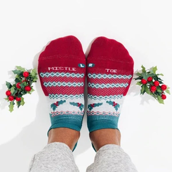Feet adorned in Feetures Elite Light Cushion festive socks with &quot;FEETURES NO SHOW SOCKS MISELTOE - WOMENS&quot; written on them, surrounded by holly sprigs.
