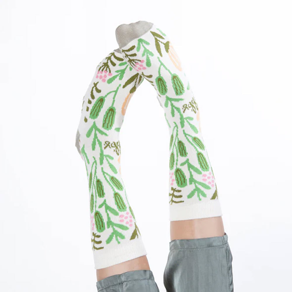 A person standing with their hands together above their head, wearing Worlds Softest socks patterned with cacti on their arms, made in USA through the AWAKE partnership to support at-risk women and children.