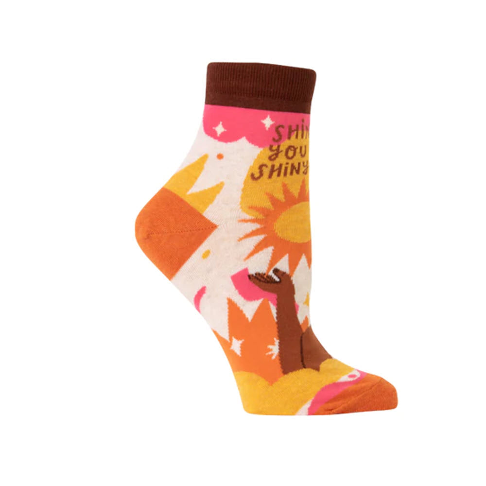 A colorful Blue Q Shine On ankle sock with a sun and mountain design and the text "shine your shins.