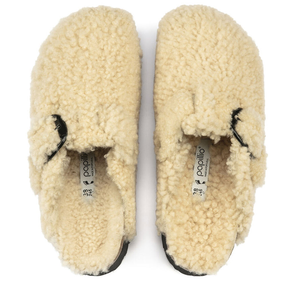 A pair of cream-colored, genuine Birkenstock shearling slippers with visible brand tags on the insoles, photographed from above on a white background.