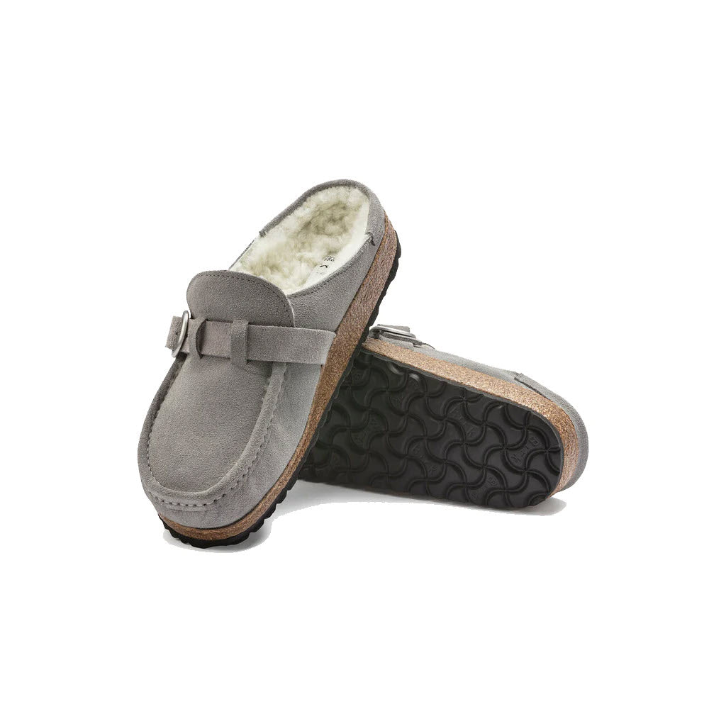 A pair of gray Birkenstock Buckley Shearling Stone Coin clog-style slippers with buckle details and fleece lining, isolated on a white background.