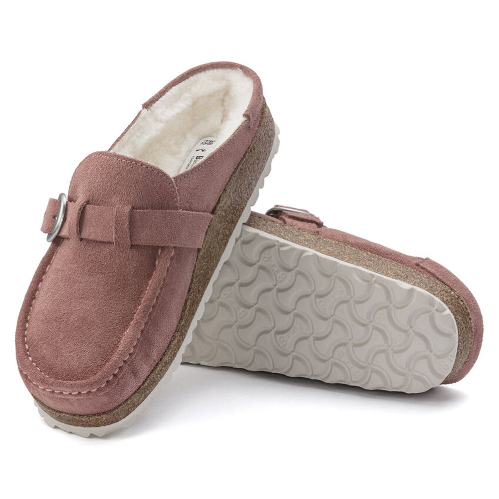 A pair of pink clay shearling Birkenstock Buckley slippers with fleece lining and a rubber sole, displayed on a white background.