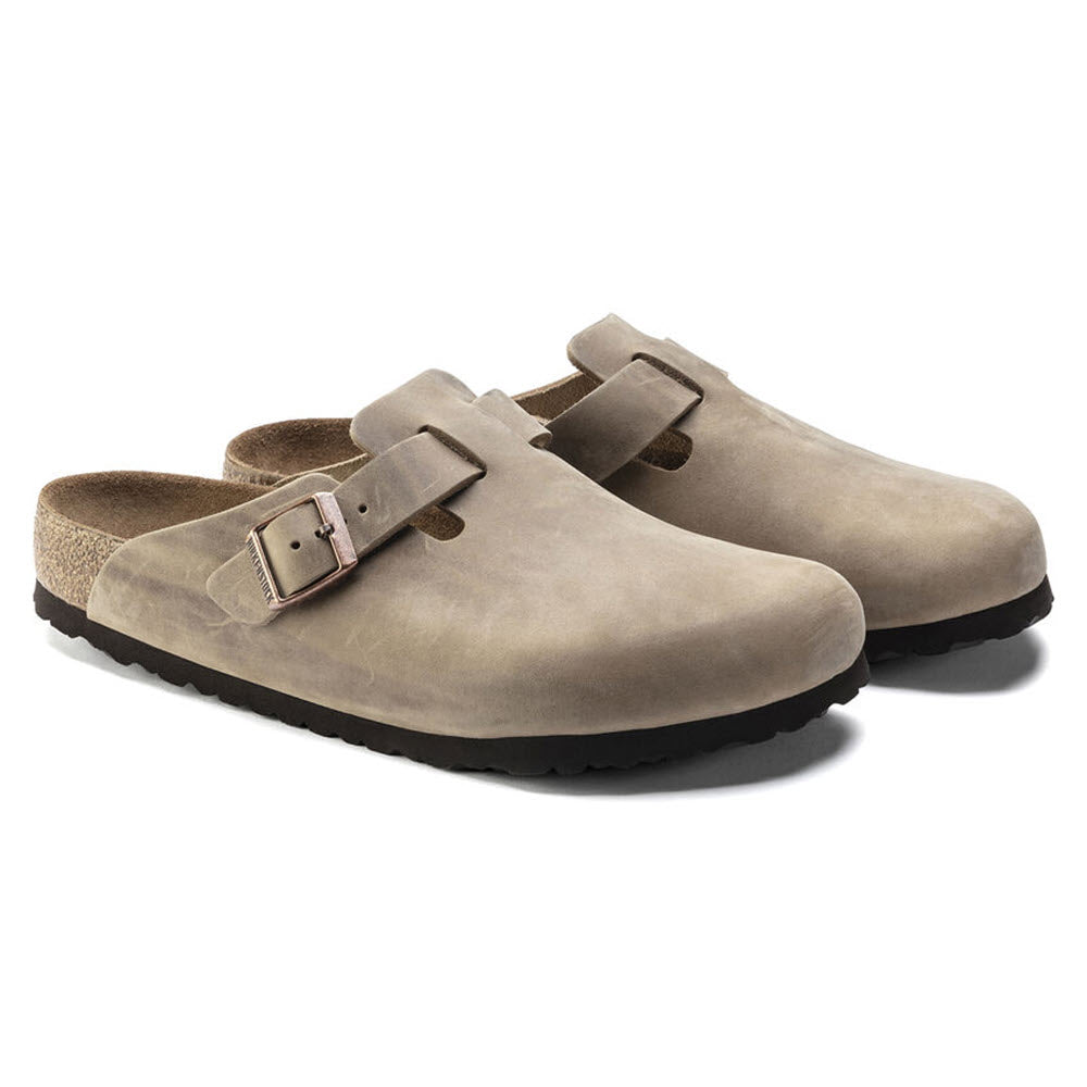 A pair of beige oiled nubuck leather Birkenstock Boston Tobacco leather clogs with buckle straps and dark soles on a white background.