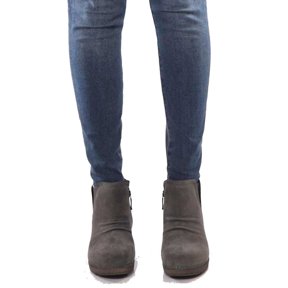 A person wearing blue jeans and a grey Dansko Caley bootie standing against a white background.