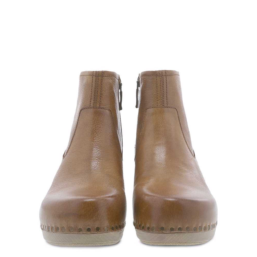 A pair of Dansko Sarah Tan Milled Burnished ankle boots with zippers at the back and decorative stitching on the soles, featuring a lightweight PU outsole, isolated on a white background.