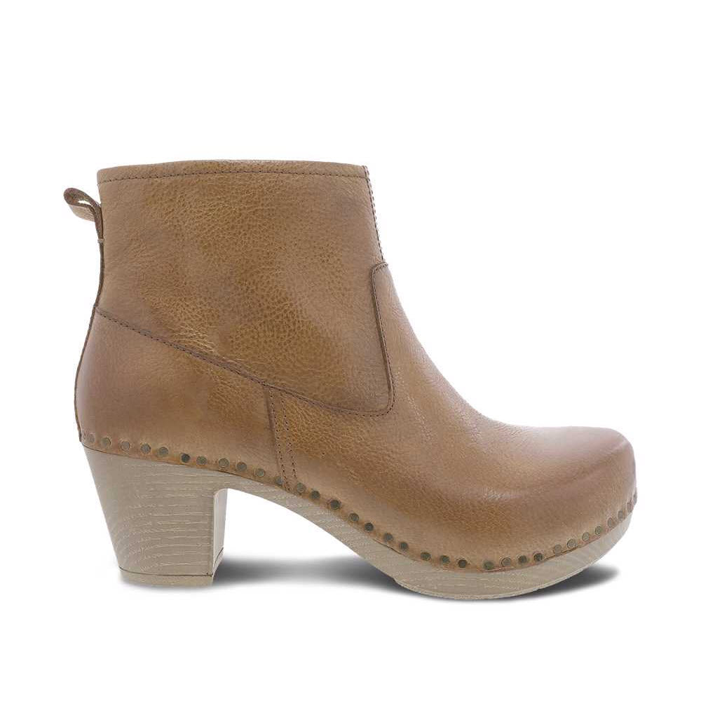 A stylish Dansko tan leather ankle bootie with a chunky heel and decorative stitching, isolated on a white background.