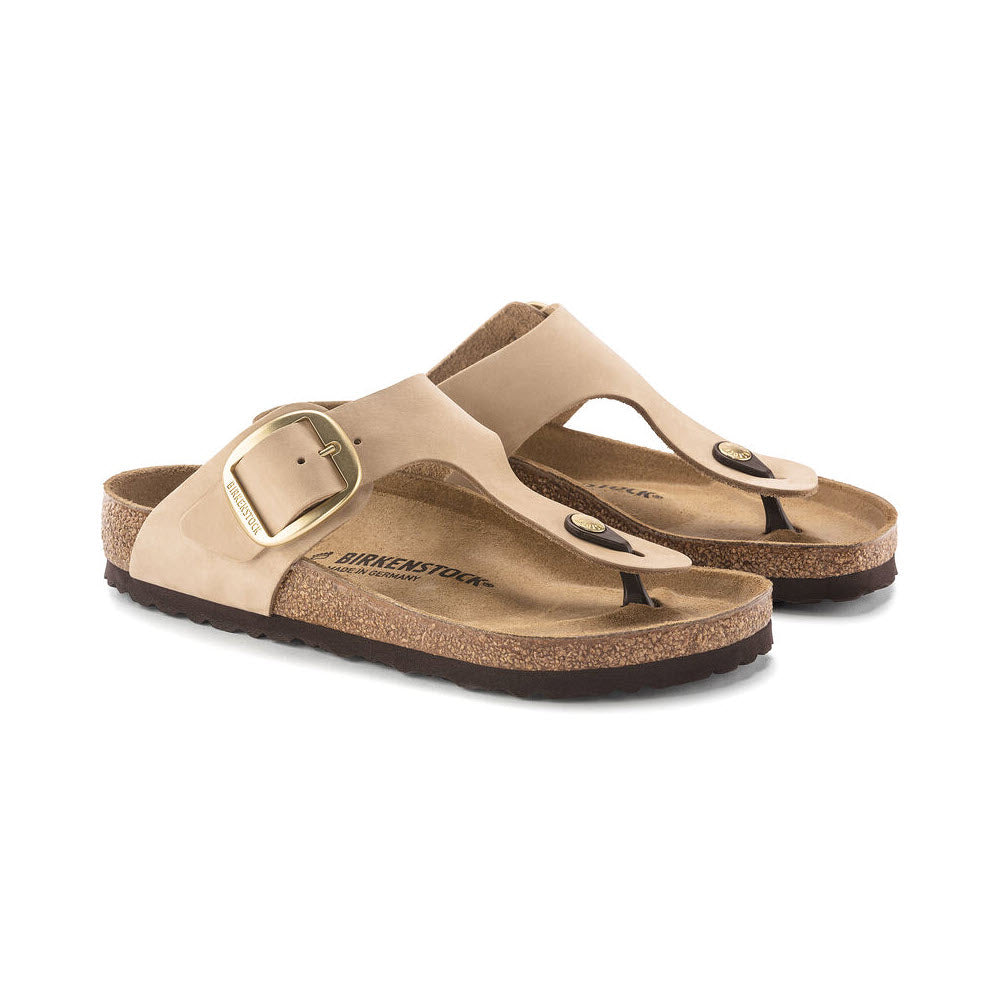 A pair of Birkenstock Gizeh Big Buckle Sandcastle sandals with beige nubuck leather straps and buckles, set against a white background.