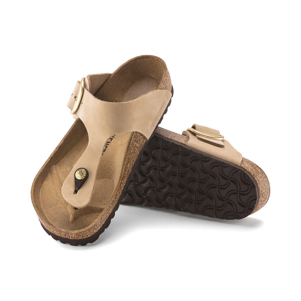 A pair of Birkenstock Gizeh Big Buckle Sandcastle - Womens with buckles and a contoured cork footbed on a white background.