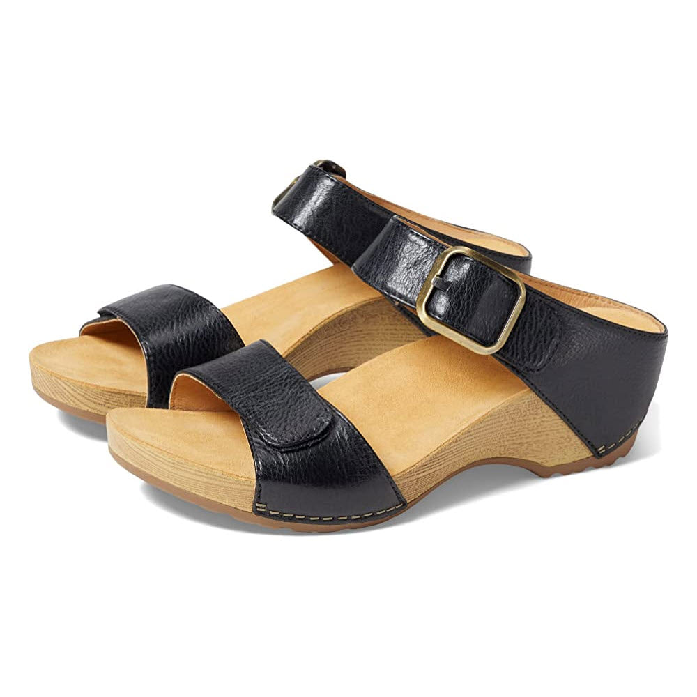 A pair of Dansko Tanya black burnished leather upper sandals with buckles on a wooden sole, viewed from the side on a white background.