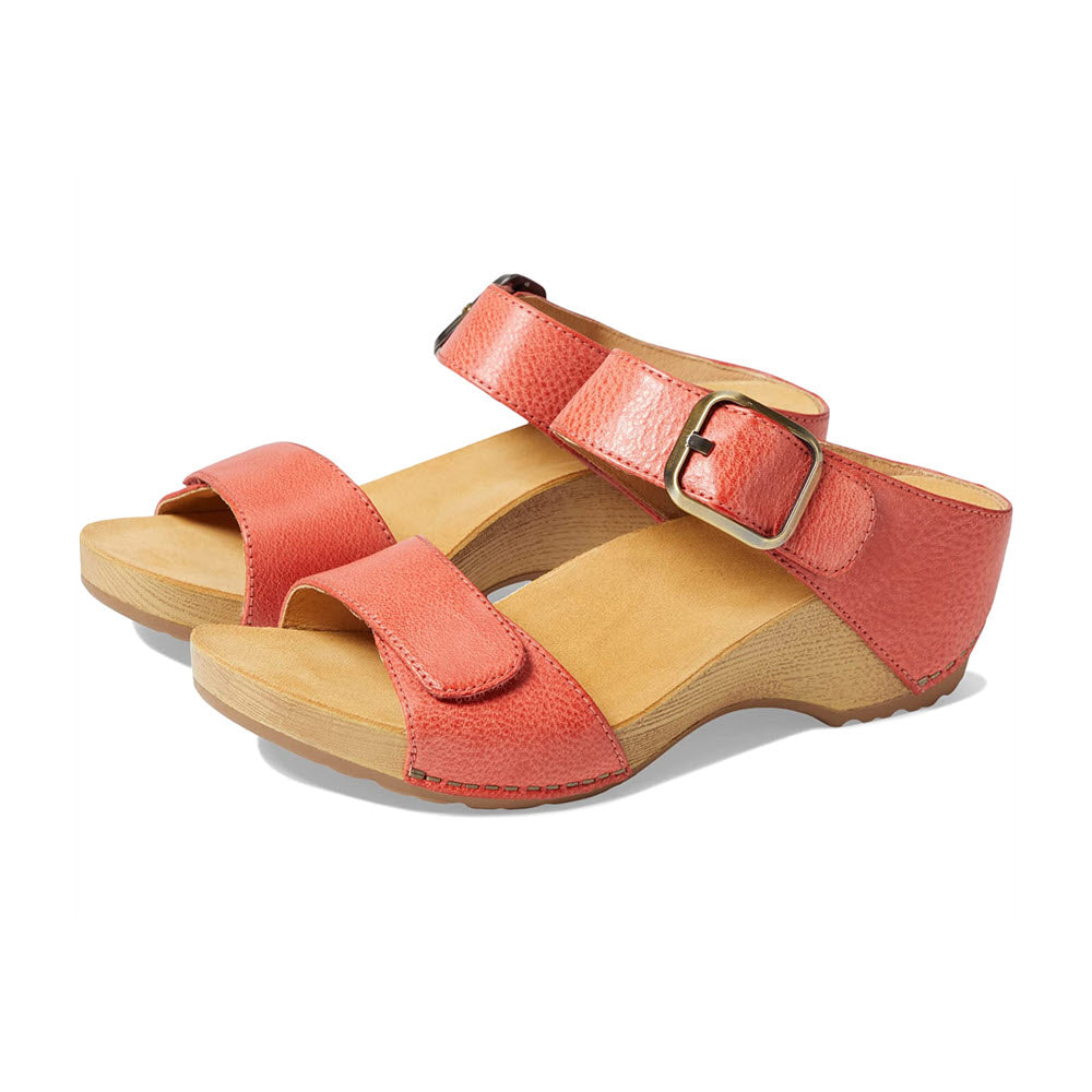 A pair of coral red Dansko Tanya Double Strap Slide Sandals with burnished leather upper, thick straps, adjustable buckle, and a slight wedge cork sole, isolated on a white background.
