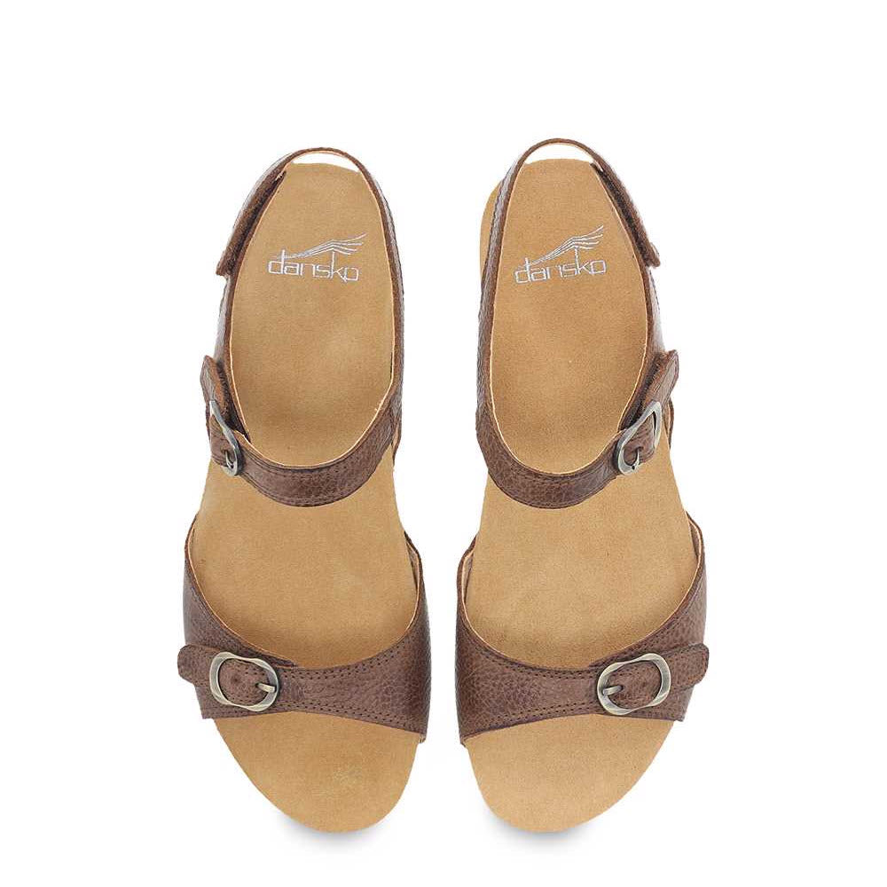 A pair of brown Dansko Tricia sandals with memory foam footbed and buckles, viewed from above on a white background.