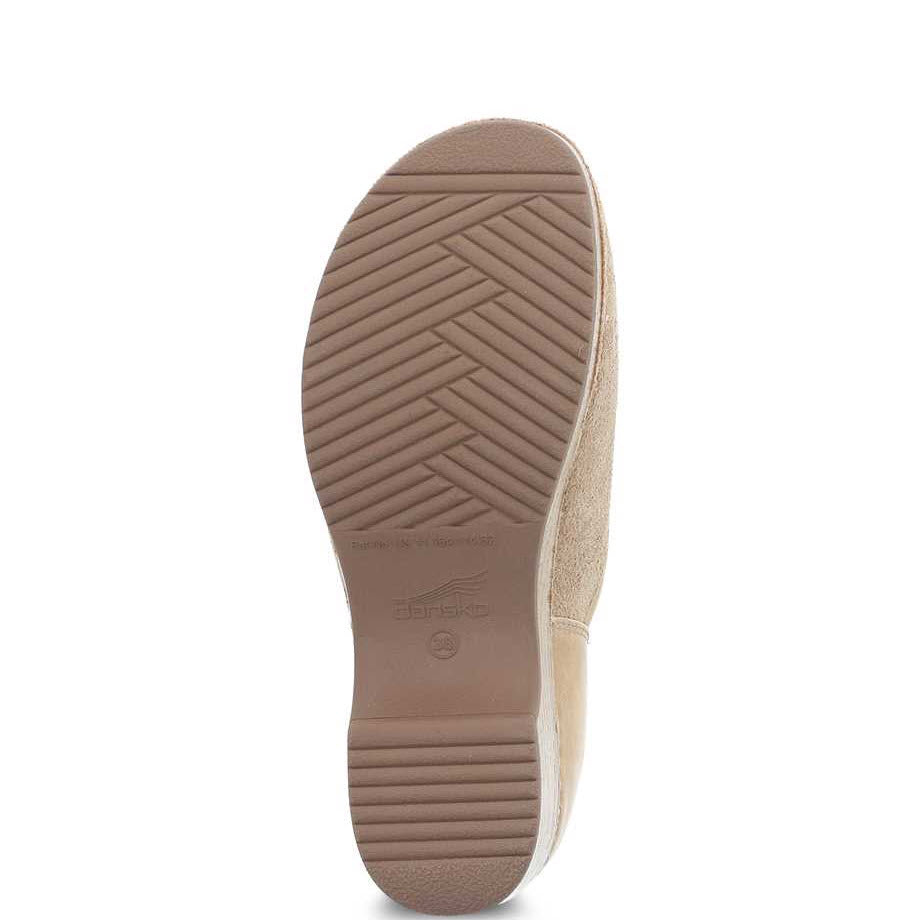 Sole of a beige Dansko Brenna Sand Suede slip on shoe displaying a herringbone tread pattern and branding.