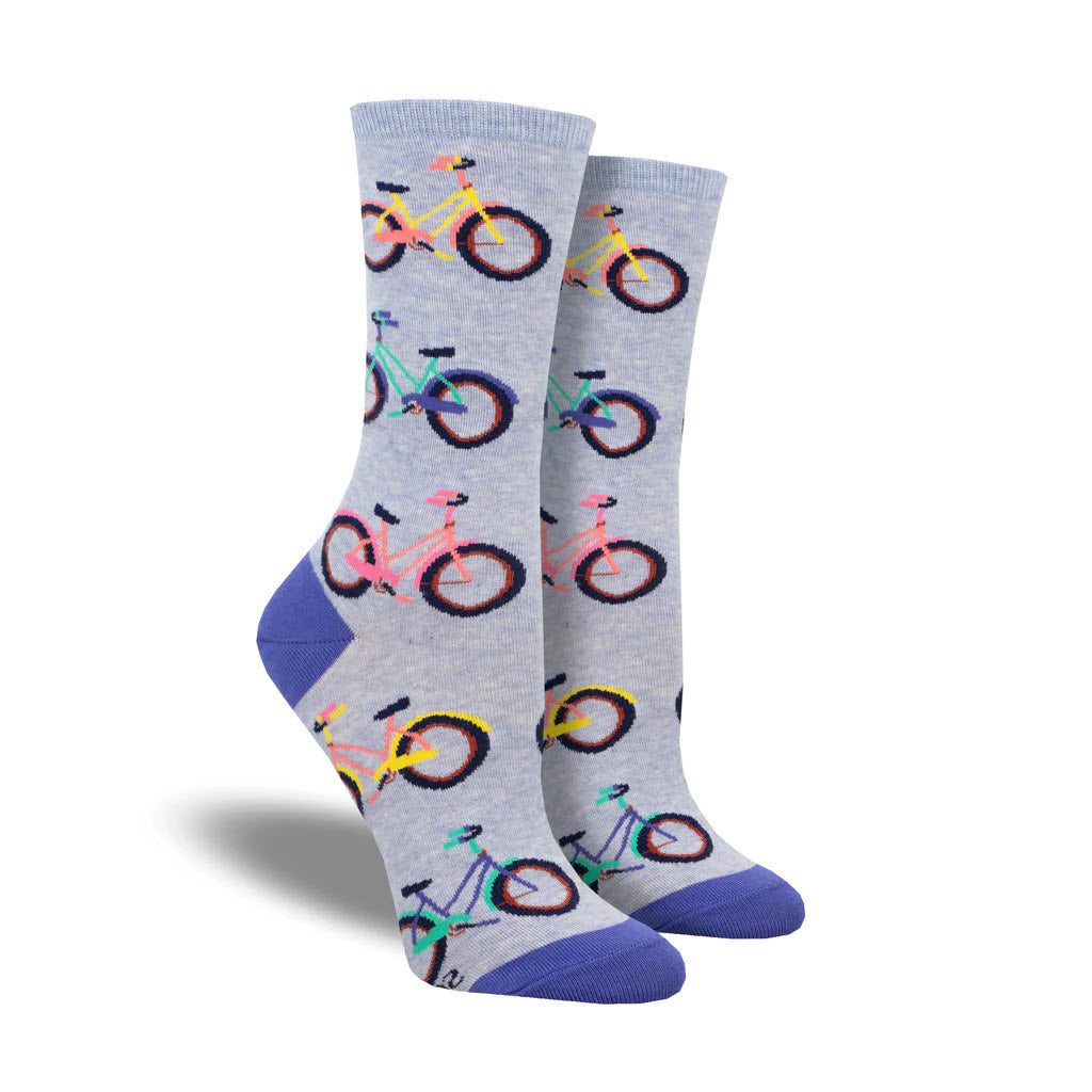 A pair of SOCKSMITH COASTAL CRUISER CREW SOCKS PERIWINKLE with a colorful bike pattern on a light gray background, featuring blue heel and toe areas.
