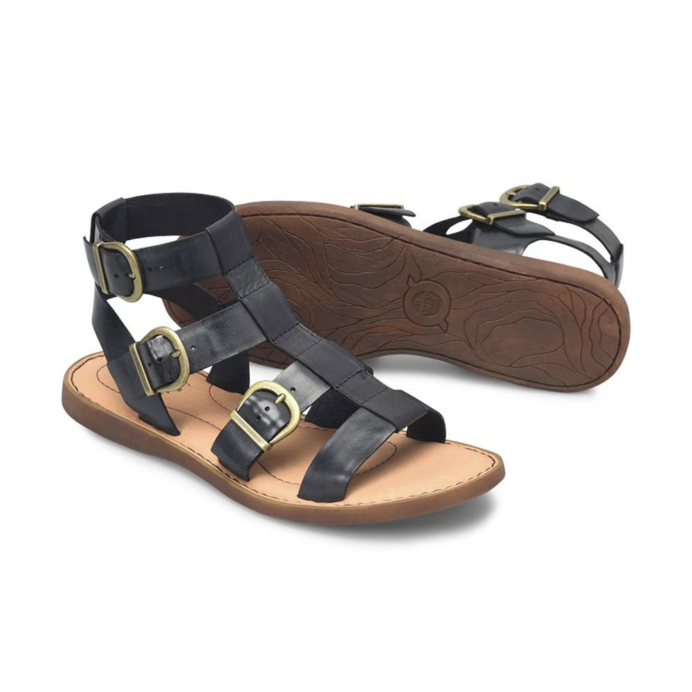 A pair of BORN HAIDEE BLACK - WOMENS gladiator sandals with buckle closures and a flat brown sole, isolated on a white background.
