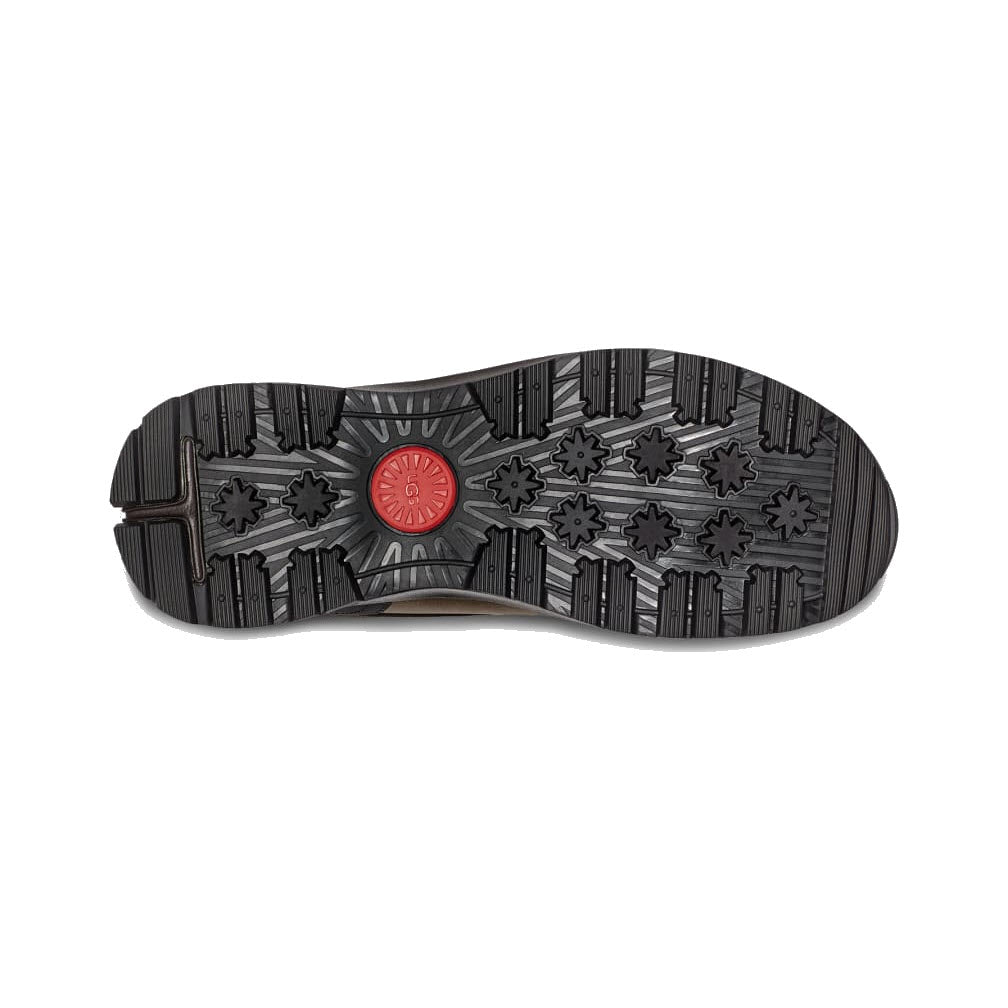 Bottom view of an Ugg shoe showing a detailed black waterproof leather sole with various grip patterns and a red circular logo in the center.
