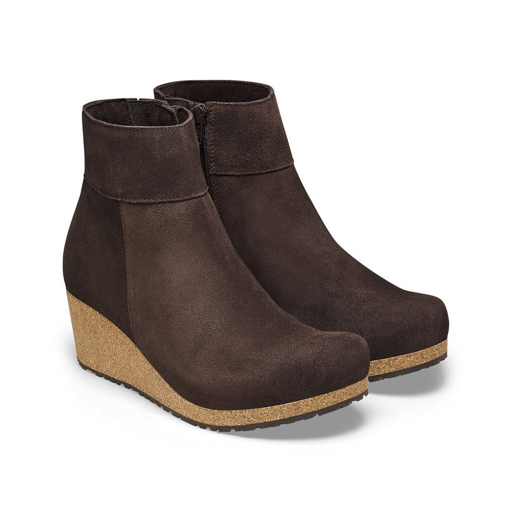 A pair of dark brown suede Birkenstock Papillio Ebba ankle boots with cork wedge heels, isolated on a white background.