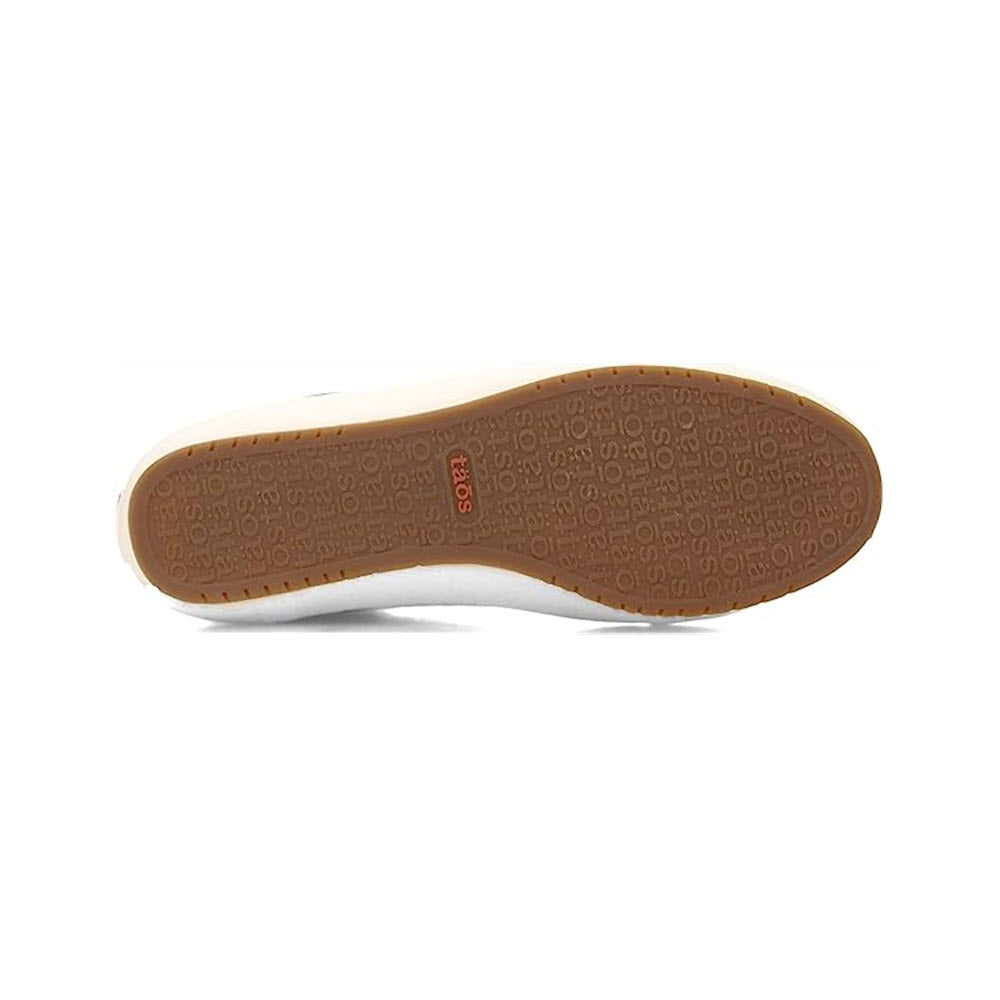 Close-up view of the bottom of a Taos shoe featuring a tan sole with embossed text and numerical patterns, fabricated from leather.