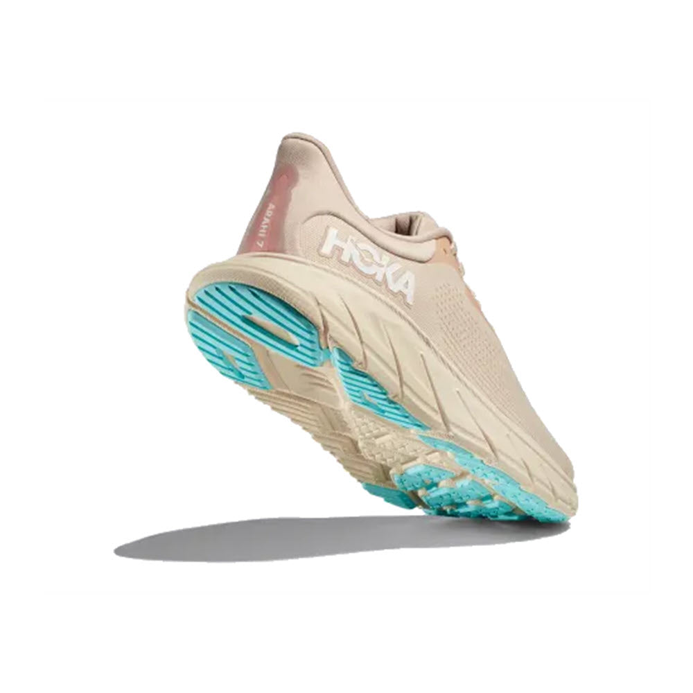 A vanilla/cream Hoka Arahi 7 stability shoe with visible branding and bright teal soles, tilted to show the tread, against a white background.