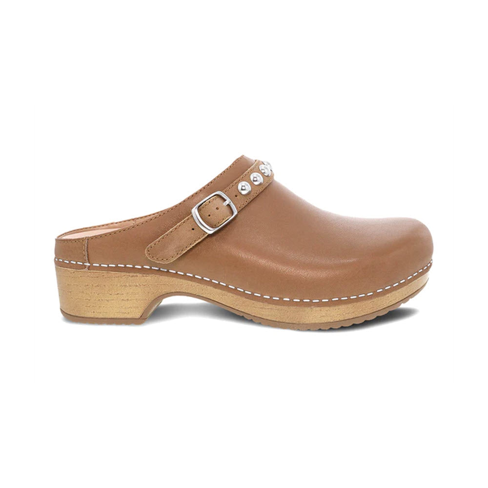 A tan leather Dansko Britton mule with silver hardware, featuring a wooden sole and visible stitching, isolated on a white background.