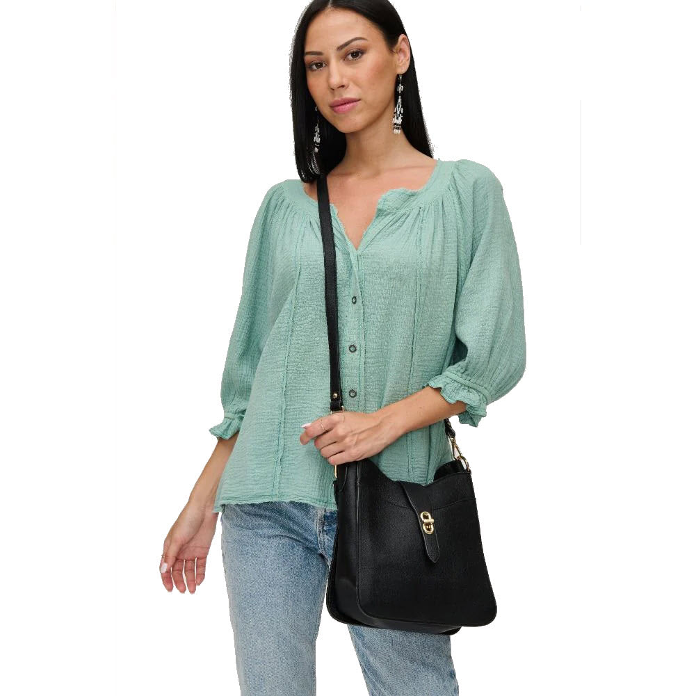 Woman in a teal blouse and jeans, carrying an URBAN EXPRESSIONS RUBY BLACK crossbody bag, standing against a white background.