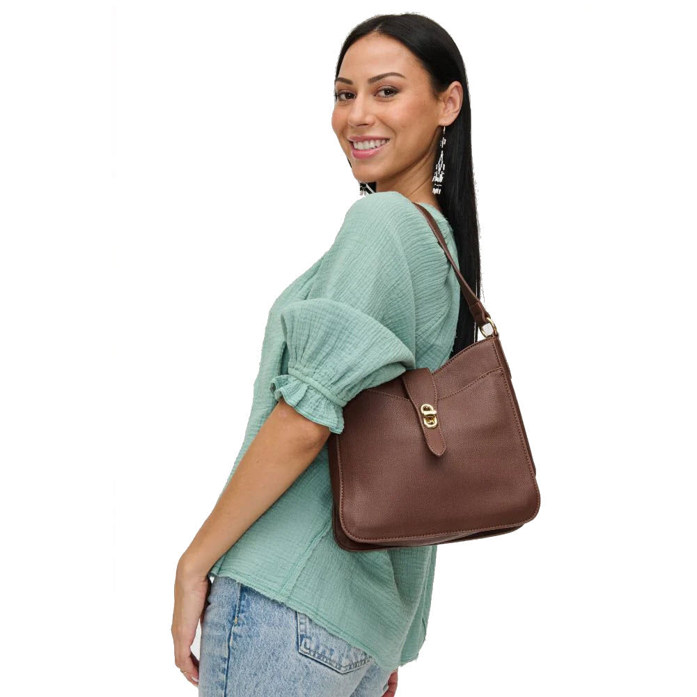 Woman in a teal top and jeans, smiling over her shoulder, wearing an URBAN EXPRESSIONS RUBY CHOCOLATE vegan leather crossbody bag.