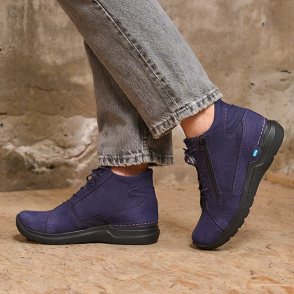 A person wearing Wolky Why Antique Nubuck Purple shoes with a lightweight PU sole and grey jeans stands on a concrete floor.